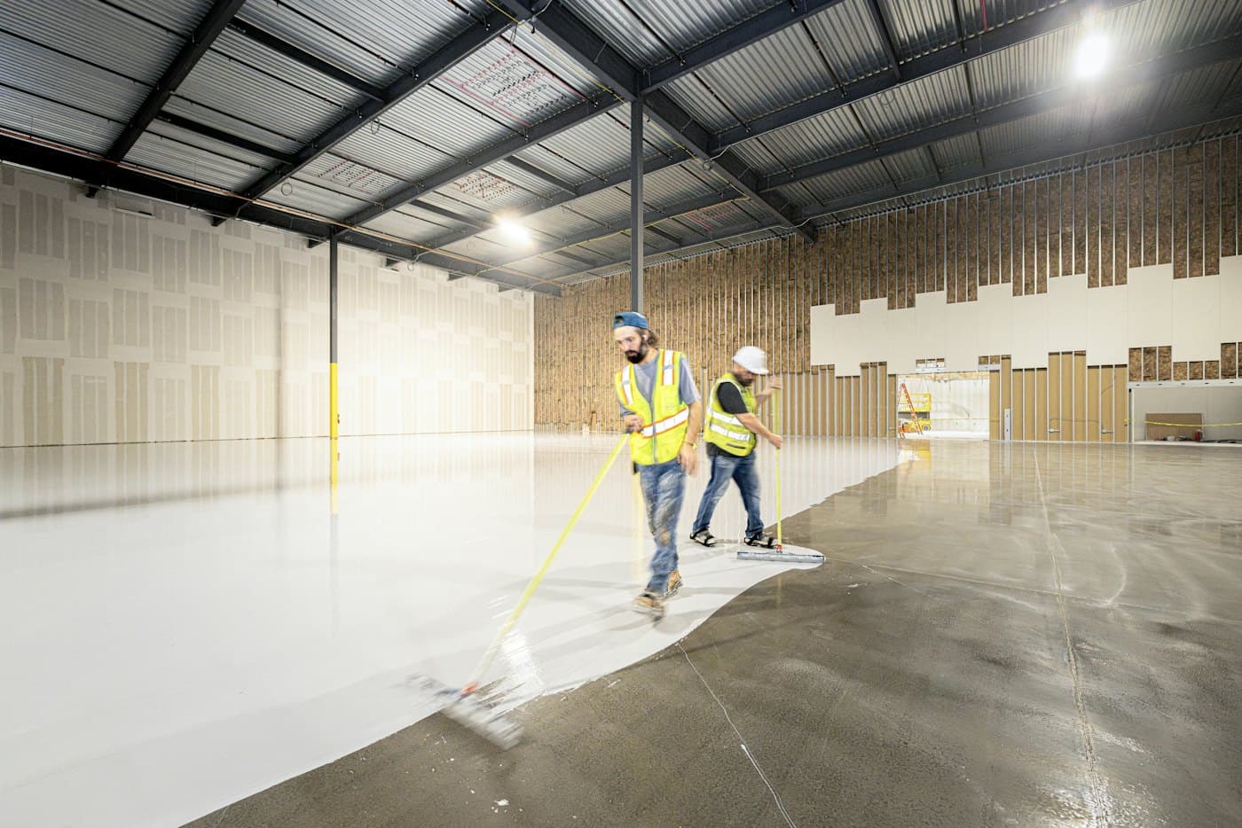 Workers applying epoxy coating to a large warehouse floor