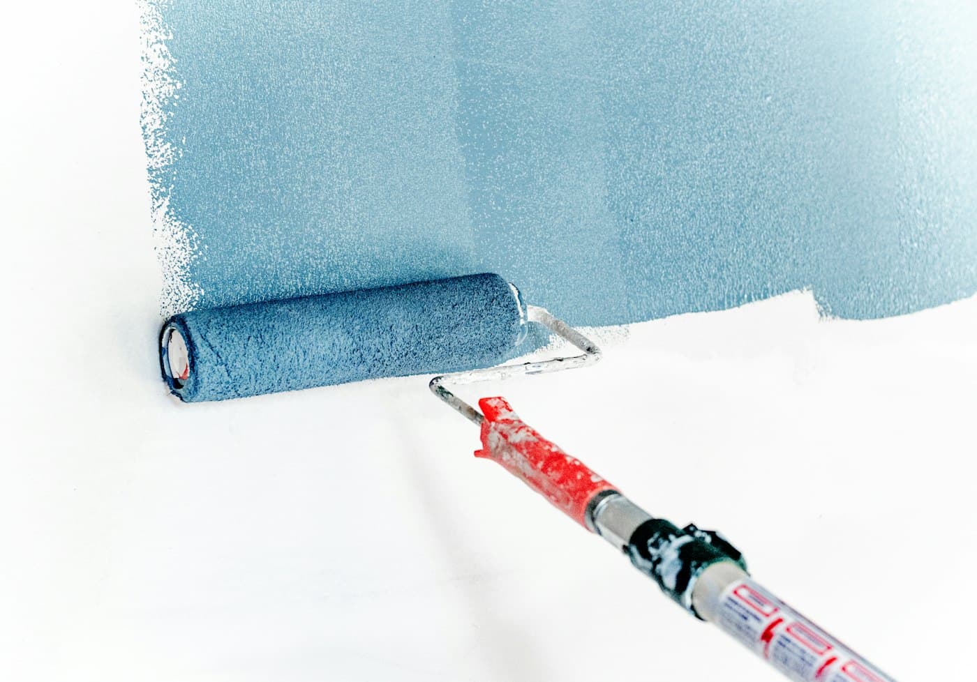 Paint roller applying fresh blue paint on a white wall